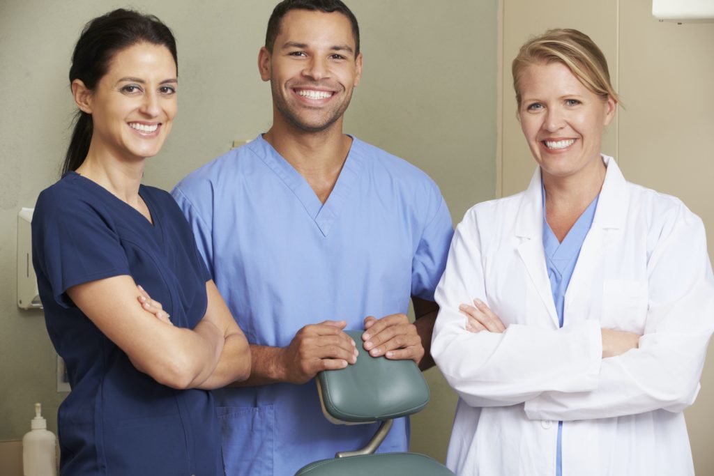 3 dentists standing around dental chair